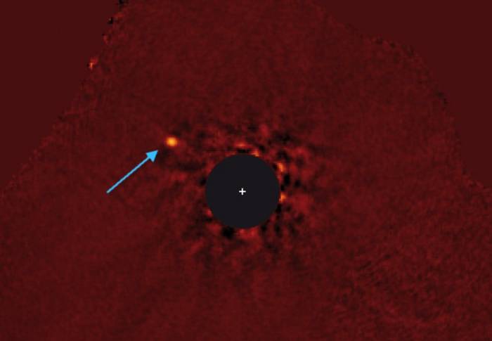 Стрелкой указано на экзопланету Каппа Андромеды b. Снимок выполнен в инфракрасном диапазоне. Звезда системы закрыта черным кругом. 
